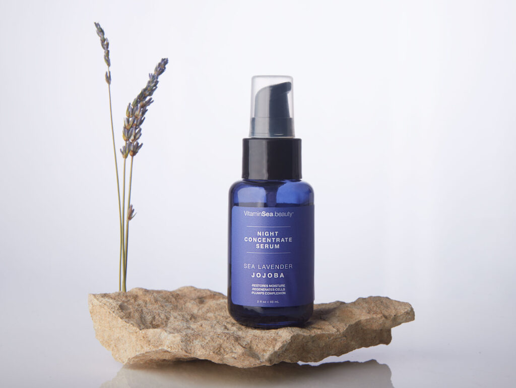 A professional picture of a night serum bottle set up in a modern and minimalistic scene on a natural stone with a stem of real lavender